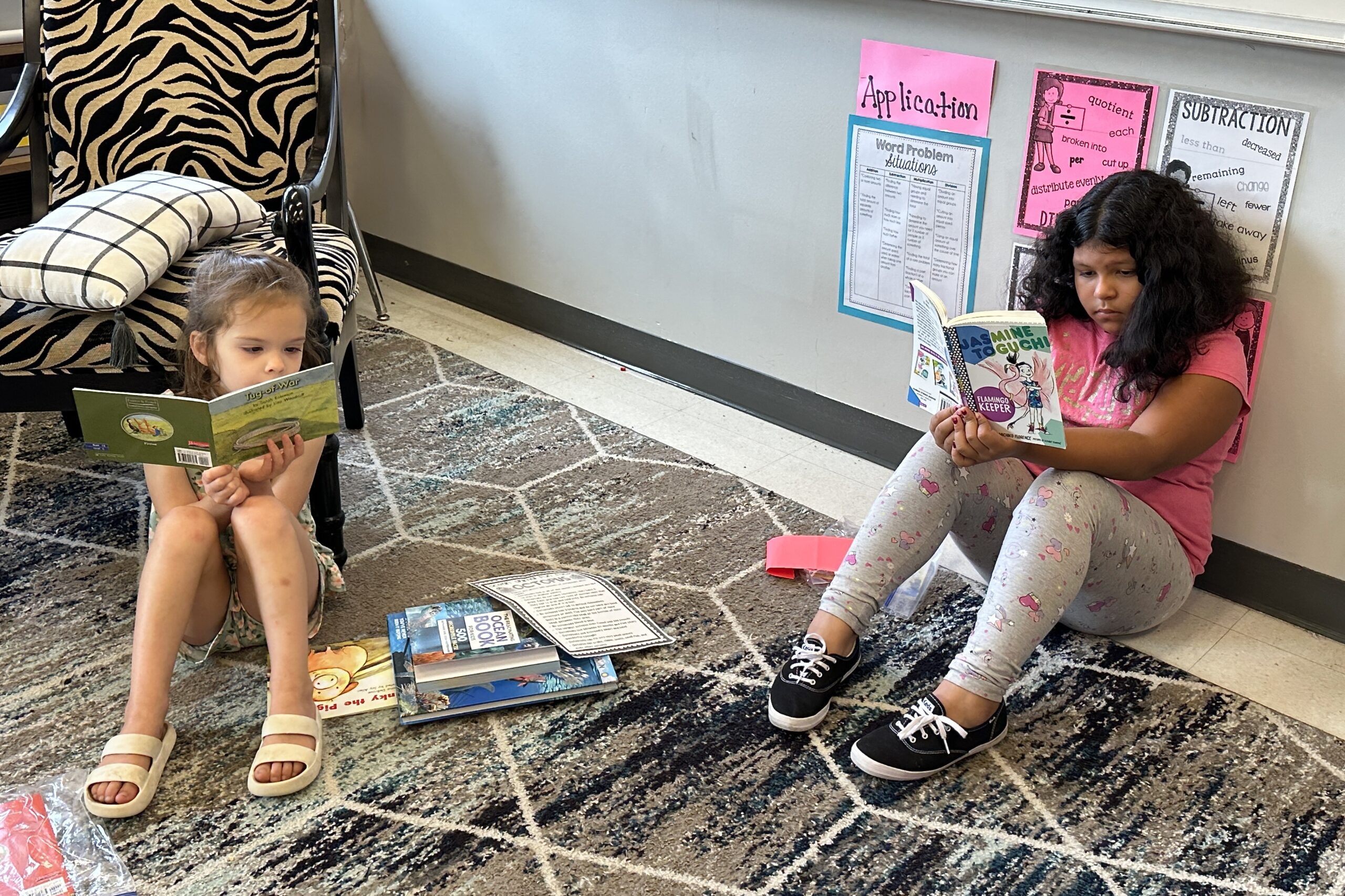 2 girls sit near each other on the carpet and read independently.